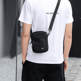sacoche bandoulière noire portée par homme en tee-shirt blanc qui est de dos